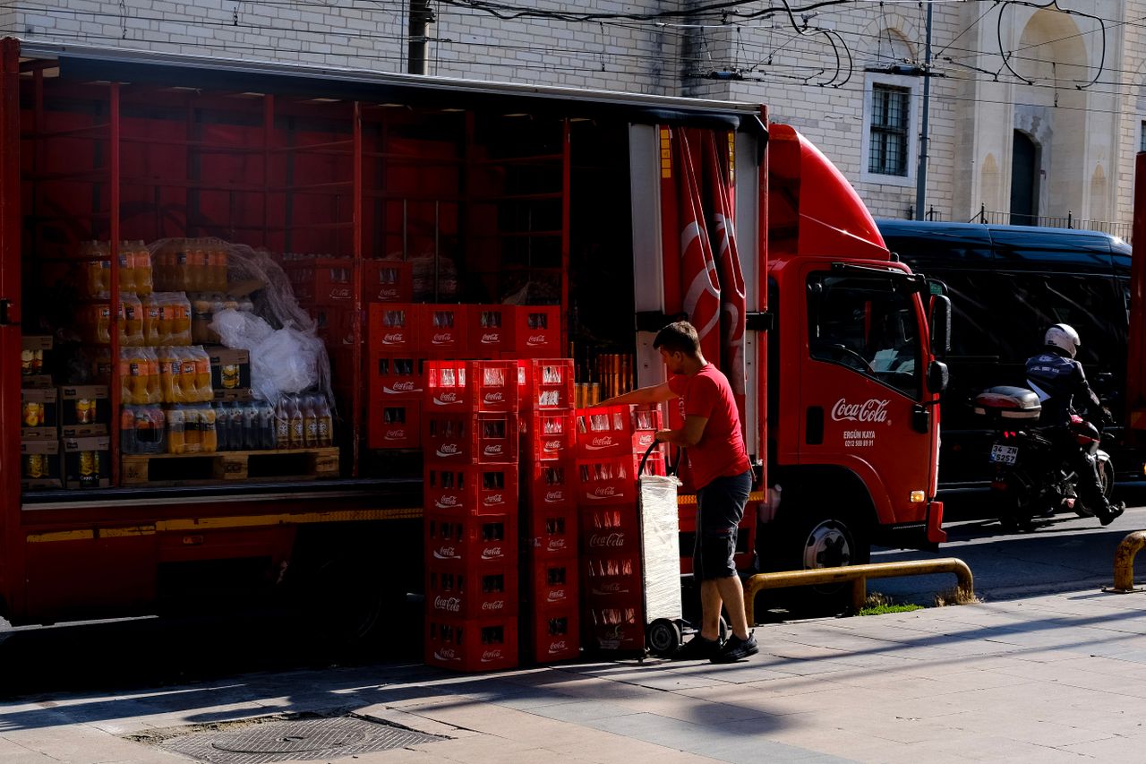 About Delivery worker unloading Coca Cola crates from truck on city street, showcasing beverage supply logistics.