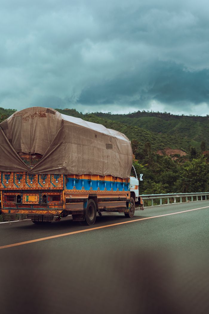 Services A vibrant truck travels on a road with lush greenery and cloudy skies, conveying a sense of journey.