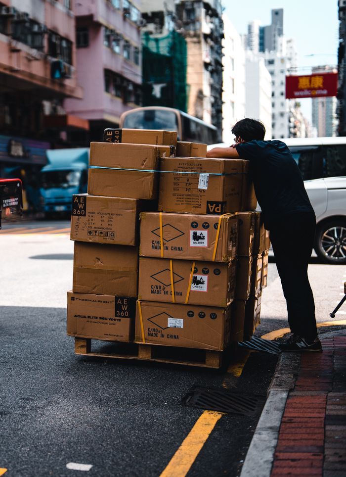 Services Man handling stacked boxes on a pallet in busy urban street scene.